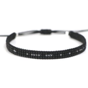 Könnte beinhalten: Schwarzes Perlenarmband mit Schiebeknotenverschluss. Das Armband besteht aus kleinen, quadratischen schwarzen Perlen mit einem Muster aus silbernen Perlen. Die verstellbare Kordel ist schwarz und weiß.