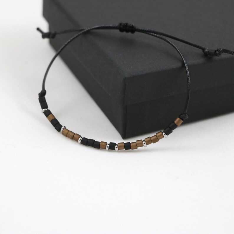 Peut inclure: Un bracelet en perles noires et dor&eacute;es avec un cordon noir.