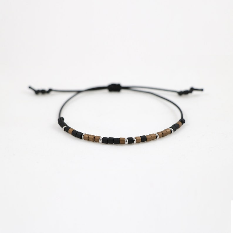 Peut inclure: Un bracelet en cordon noir avec des perles carr&eacute;es brunes et argent&eacute;es.