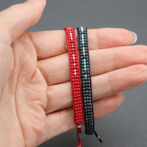 May include: Two beaded bracelets, one red with white accents and one black with turquoise accents.