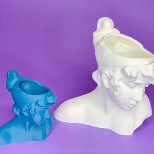 May include: Two white ceramic planter busts, one is blue and the other is white. Both have a hollow top for planting.