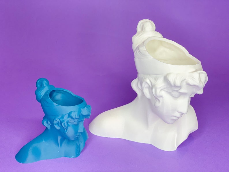 May include: Two white ceramic planter busts, one is blue and the other is white. Both have a hollow top for planting.