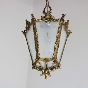 Puede incluir: Una linterna de metal dorado con una pantalla de vidrio transparente que presenta un diseño de estrella. La linterna tiene detalles ornamentados y un remate decorativo.