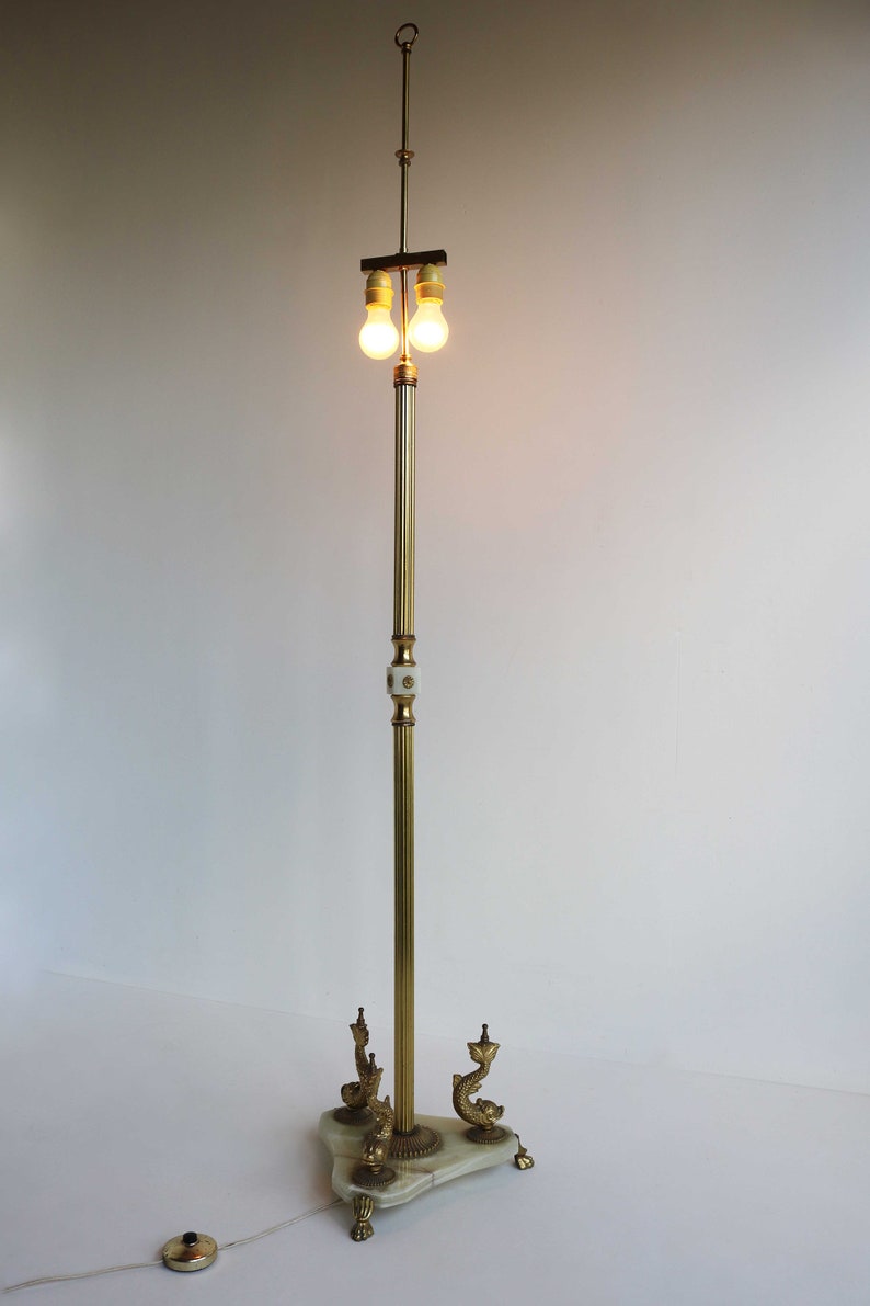 May include: A vintage brass floor lamp with two light bulbs. The lamp features a marble base with decorative dolphin accents. The lamp's height is approximately 60 inches.