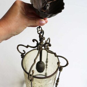 Pode incluir: Um candeeiro de teto vintage em lat&atilde;o e vidro com um abajur de vidro fosco e trabalhos em metal ornamentados. O candeeiro de teto tem uma corrente e uma tampa de metal decorativa.