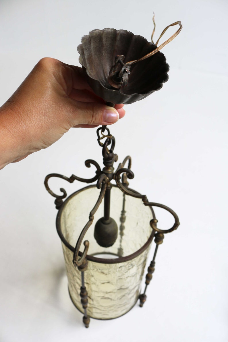 Pode incluir: Um candeeiro de teto vintage em lat&atilde;o e vidro com um abajur de vidro fosco e trabalhos em metal ornamentados. O candeeiro de teto tem uma corrente e uma tampa de metal decorativa.