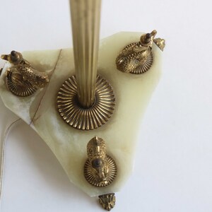 May include: A vintage wall sconce featuring a light green onyx base with brass accents. The sconce has a central brass rod and is adorned with three brass ram's head details. A power cord extends from the base.