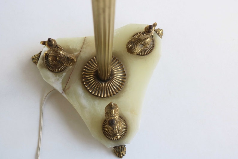 May include: A vintage wall sconce featuring a light green onyx base with brass accents. The sconce has a central brass rod and is adorned with three brass ram's head details. A power cord extends from the base.