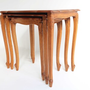 Peut inclure: Un ensemble de trois tables gigognes avec des sculptures complexes sur les pieds. Les tables sont en bois brun clair et ont un design simple et élégant.
