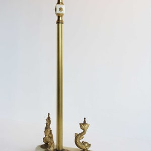 May include: A vintage brass floor lamp with a fluted pole and decorative dolphin base. The lamp features a white marble base and ornate detailing. The lamp's height is approximately 60 inches.