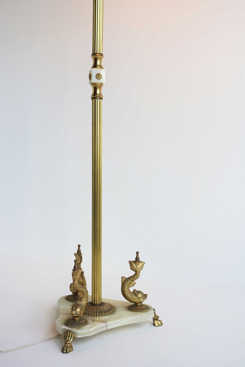 May include: A vintage brass floor lamp with a fluted pole and decorative dolphin base. The lamp features a white marble base and ornate detailing. The lamp's height is approximately 60 inches.
