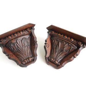May include: A pair of dark brown wooden wall shelves with intricate carved details. The shelves are shaped like a half-circle and have a decorative border around the top.