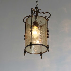 Pode incluir: Um candeeiro pendente de estilo vintage com um abajur de vidro transparente texturizado e uma estrutura de metal. A luz est&aacute; pendurada numa corrente e tem uma l&acirc;mpada incandescente quente.