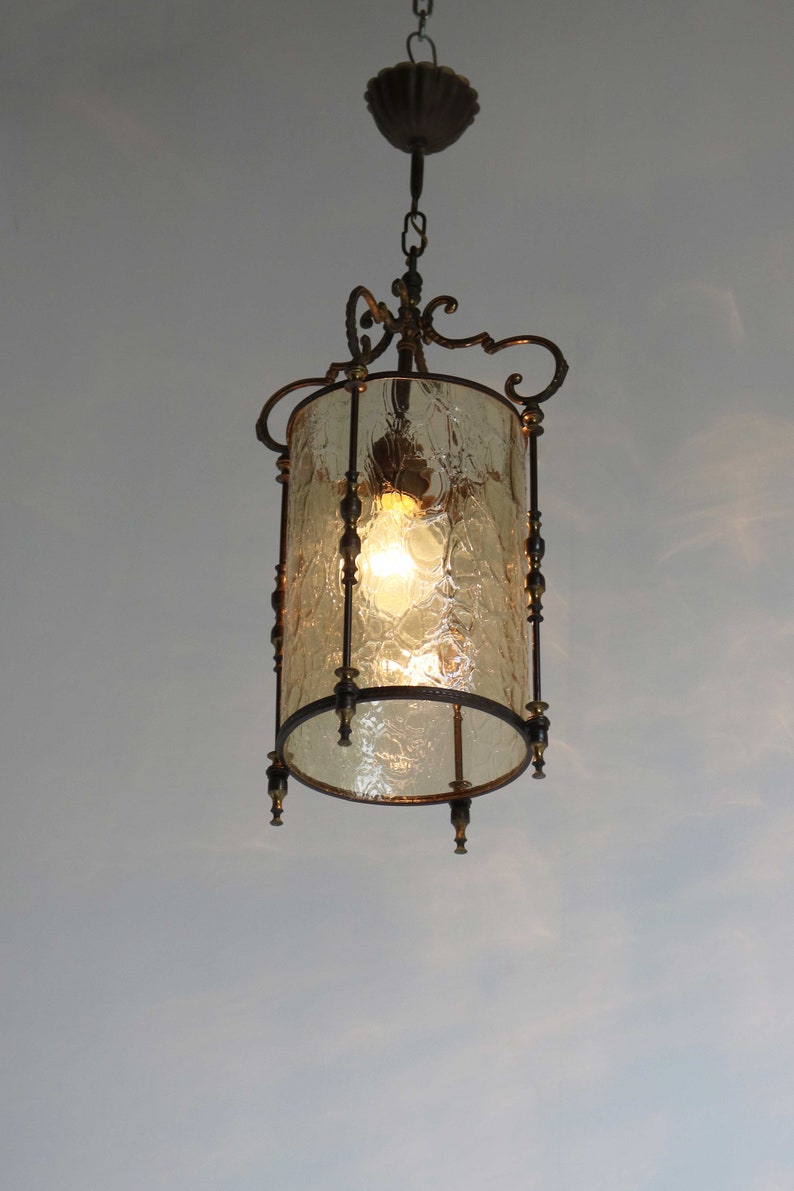 Pode incluir: Um candeeiro pendente de estilo vintage com um abajur de vidro transparente texturizado e uma estrutura de metal. A luz est&aacute; pendurada numa corrente e tem uma l&acirc;mpada incandescente quente.