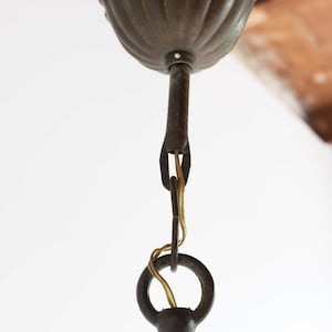 Pode incluir: Close-up de uma montagem de teto de candeeiro de bronze com um dossel decorativo em forma de concha. A montagem tem uma corrente e um anel para pendurar o candeeiro.