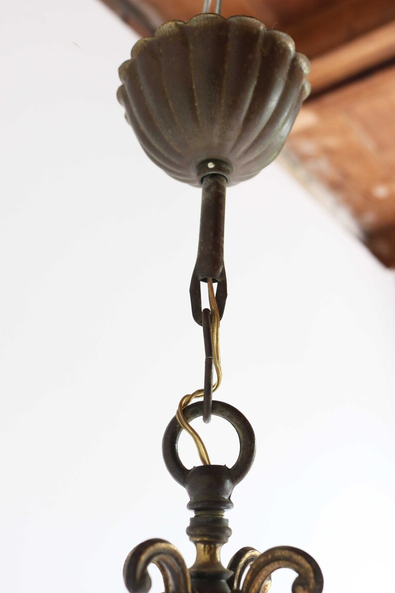 Pode incluir: Close-up de uma montagem de teto de candeeiro de bronze com um dossel decorativo em forma de concha. A montagem tem uma corrente e um anel para pendurar o candeeiro.