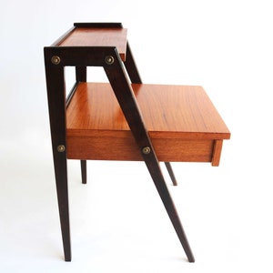Può includere: Un tavolino da salotto in stile moderno di metà secolo con un cassetto e uno scaffale. Il tavolo è in legno con una finitura marrone scuro e ha gambe inclinate.