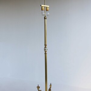 May include: A vintage brass floor lamp with a marble base and dolphin accents. The lamp features a slender, adjustable pole with two light bulbs. The base has a triangular shape with decorative feet. The lamp is approximately 60 inches tall.
