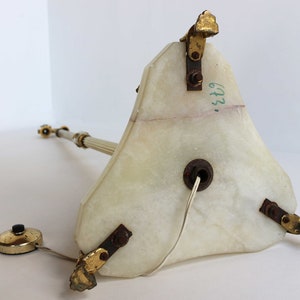 May include: A vintage table lamp with a triangular, off-white marble base and a slender, fluted column. The lamp features gold-toned metal accents and a foot switch. The lamp's base has a visible crack and the number "673" is written on the side.