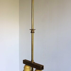 May include: A vintage brass floor lamp with a ring at the top and two light bulb sockets. The lamp has a long, slender pole and a rectangular bar holding the sockets. The sockets are a light yellow color.