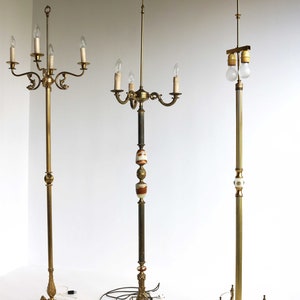 May include: Three antique floor lamps with ornate brass and marble bases. The lamps feature multiple light fixtures with candelabra-style bulbs. The lamps have a vintage aesthetic, with detailed metalwork and decorative elements.