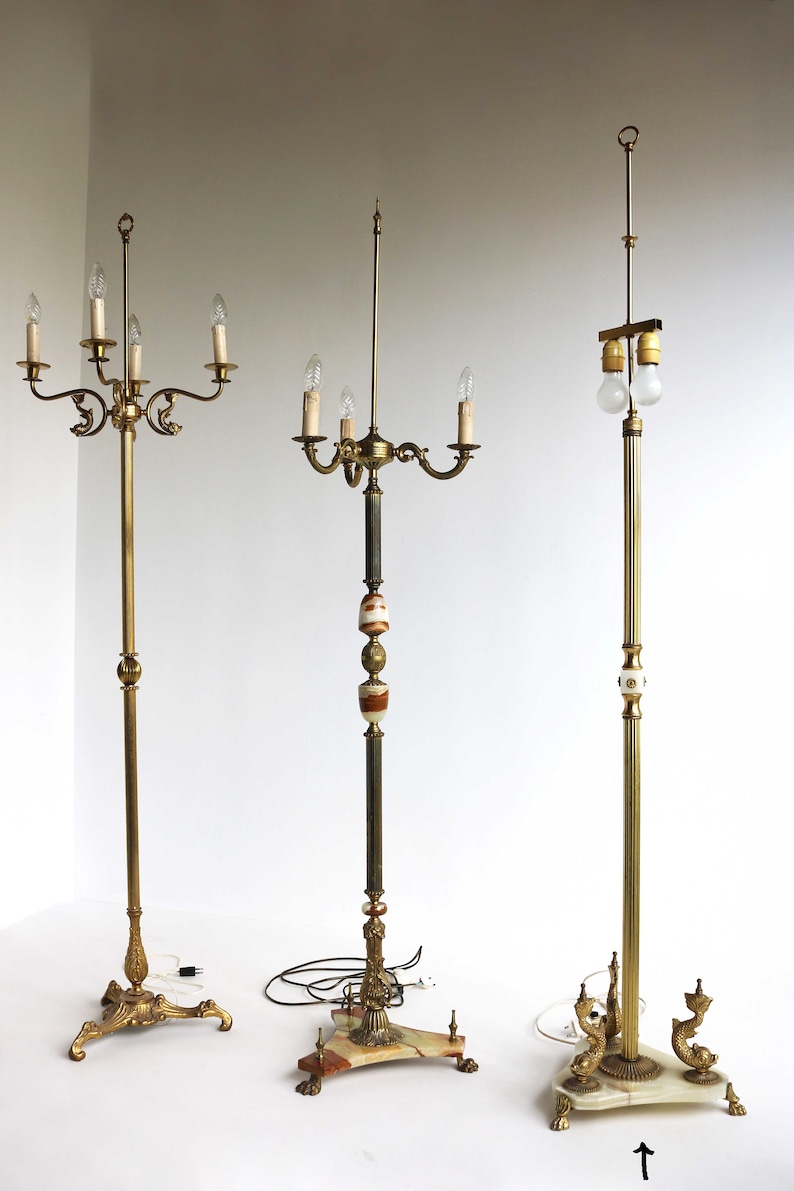 May include: Three antique floor lamps with ornate brass and marble bases. The lamps feature multiple light fixtures with candelabra-style bulbs. The lamps have a vintage aesthetic, with detailed metalwork and decorative elements.