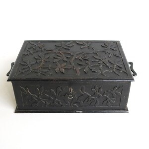 May include: A black wooden box with intricate floral carvings on the lid and sides. The box has two metal handles and a keyhole.