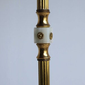 May include: A close-up of a gold-colored, fluted metal object with a white, square-shaped center. The center has gold-colored floral accents. The object has a vintage aesthetic.