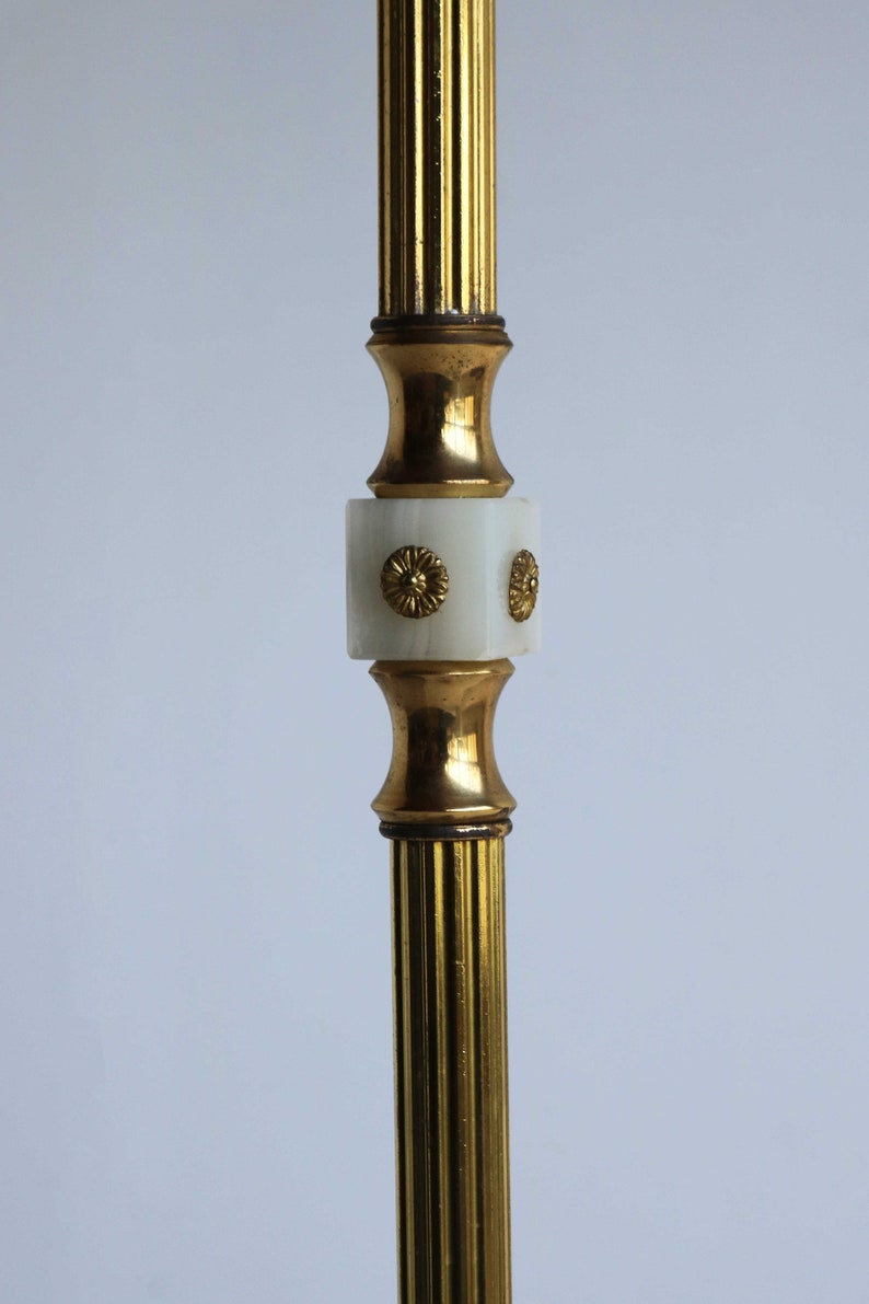 May include: A close-up of a gold-colored, fluted metal object with a white, square-shaped center. The center has gold-colored floral accents. The object has a vintage aesthetic.
