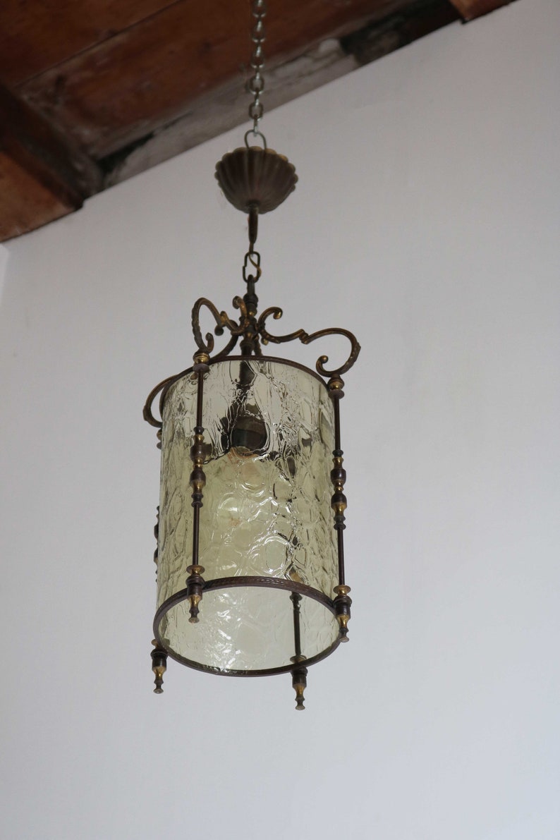 Pode incluir: Um candeeiro pendente vintage em lat&atilde;o e vidro com um abajur de vidro texturizado. O candeeiro tem um design decorativo e ornamentado com uma corrente pendurada no teto.