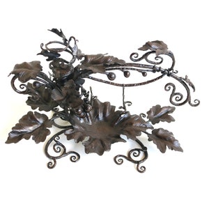 May include: A wrought iron wine rack with a grapevine design. The rack features intricate details of leaves and grapes, and a circular top for holding bottles.