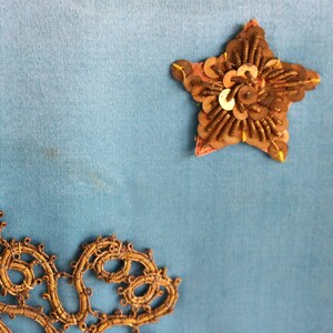 May include: A blue fabric background with a gold star-shaped embellishment and a gold lace design in the bottom left corner.