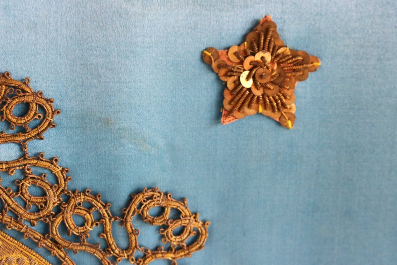 May include: A blue fabric background with a gold star-shaped embellishment and a gold lace design in the bottom left corner.