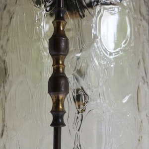 Pode incluir: Um close-up de um abajur de l&acirc;mpada vintage de vidro com uma superf&iacute;cie texturizada e com bolhas. O abajur &eacute; feito de vidro transparente e tem uma moldura de lat&atilde;o.