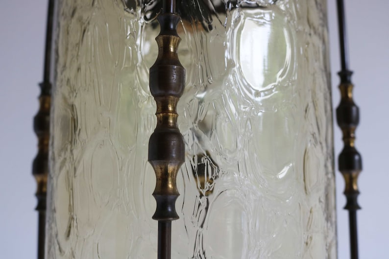 Pode incluir: Um close-up de um abajur de l&acirc;mpada vintage de vidro com uma superf&iacute;cie texturizada e com bolhas. O abajur &eacute; feito de vidro transparente e tem uma moldura de lat&atilde;o.