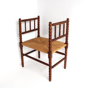 Op de afbeelding: Een vintage houten stoel met een geweven strooien zitting. De stoel heeft een donkerbruine afwerking met gedraaide spijlen op de poten en rugleuningen. De zitting is van een natuurlijke bruine kleur, tegen een witte achtergrond.