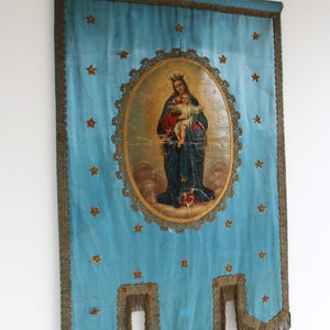 May include: A blue fabric banner with gold trim and a central image of the Virgin Mary holding a baby Jesus. The image is surrounded by a gold frame and the banner is decorated with gold stars.