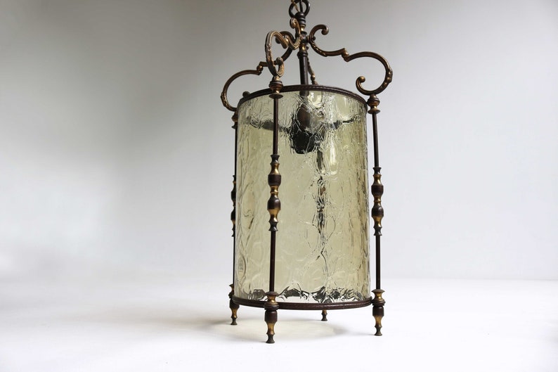 Pode incluir: Um candeeiro pendente vintage em lat&atilde;o e vidro com um abajur de vidro cil&iacute;ndrico. O vidro tem um acabamento texturizado rachado e a moldura de lat&atilde;o tem detalhes ornamentados.
