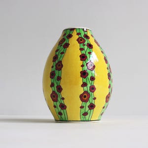 Puede incluir: Un jarrón de cerámica amarillo con un diseño floral verde y rojo. El jarrón tiene un cuerpo redondeado y un cuello estrecho.