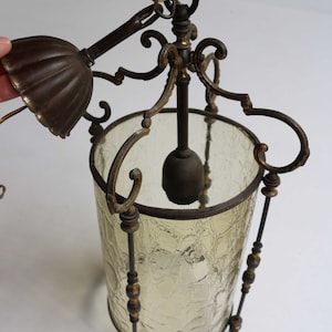 Pode incluir: Um candeeiro pendente vintage em lat&atilde;o e vidro com um abajur de vidro texturizado e trabalho de metal ornamentado. O candeeiro tem uma corrente e um gancho para pendurar.