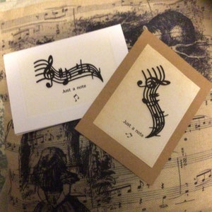 May include: Two cards featuring a musical note design and the text "Just a note". The cards are displayed on a fabric background with a musical note pattern.