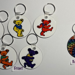 May include: Six round keychains with different designs featuring a dancing bear with a rainbow color scheme. The back of one keychain shows a swirling pattern of dancing bears. The keychains are labeled "Front" and "Back".
