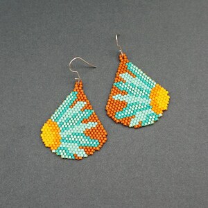 May include: A pair of teardrop-shaped earrings with a beaded design. The earrings are made with orange, yellow, and turquoise beads and feature a flower-like pattern.