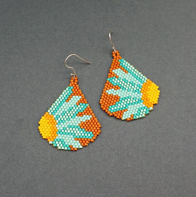 May include: A pair of teardrop-shaped earrings with a beaded design. The earrings are made with orange, yellow, and turquoise beads and feature a flower-like pattern.