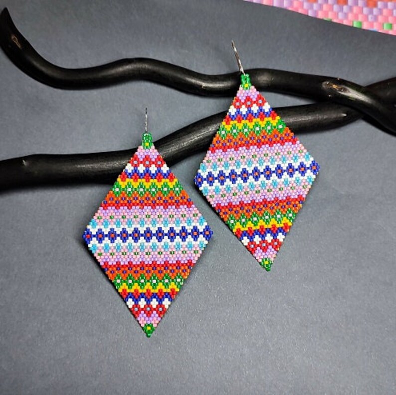 May include: A pair of colorful diamond-shaped earrings with a geometric pattern of pink, red, green, blue, and white beads.