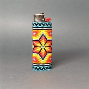 May include: A beaded lighter cover with a colorful geometric pattern featuring a large orange flower in the center. The cover is made of small, colorful beads and is designed to fit a standard-sized lighter.