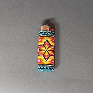 May include: A lighter with a colorful beaded cover. The cover features a geometric pattern with a star-shaped design in shades of orange, yellow, and blue.
