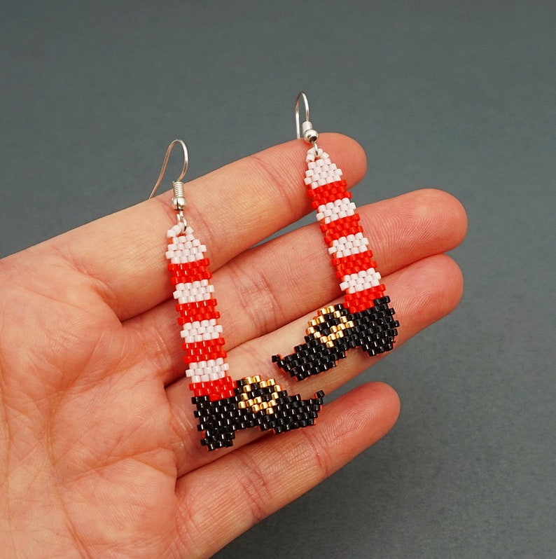 Op de afbeelding: Een paar grillige kralen oorbellen in de vorm van kerstmanbenen. De oorbellen hebben rood-wit gestreepte benen met zwarte laarzen en gouden details. De oorbellen hangen aan zilverkleurige haken.