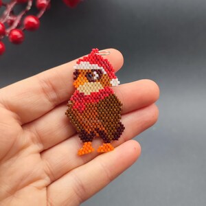 May include: A beaded owl ornament wearing a red Santa hat with white trim. The owl is brown, orange, and white.