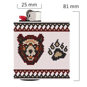 May include: A white lighter with a beaded cover featuring a brown bear face and paw print. The beads are in a geometric pattern with black, brown, and beige colors. The lighter is 25 mm wide and 81 mm tall.